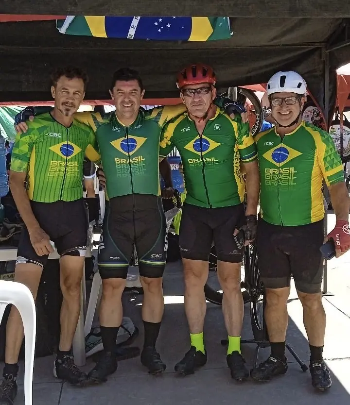 Quatro ciclistas com uniforme da Seleção Brasileira posam lado a lado sob uma tenda