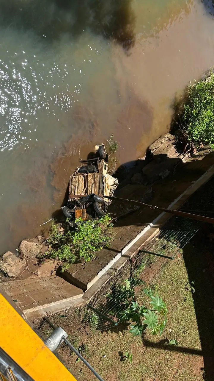 Vista de cima da carcaça do veículo no rio, perto da margem e abaixo da passarela